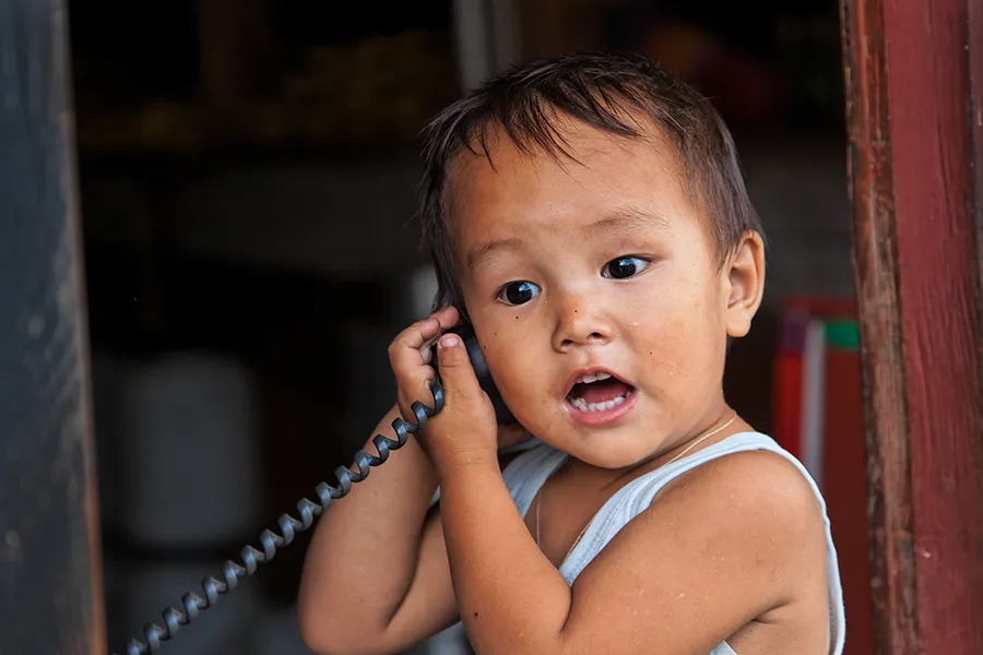 Ein asiatisches Kind hält einen Telefonhörer mit Schnur.